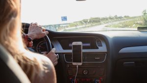 Vrouw rijdt in moderne lesauto met zicht op dashboard en smartphonescherm