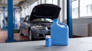Blauwe jerrycan en klein flesje vloeistof op een werkbank in een garage met een auto met open motorkap op de achtergrond